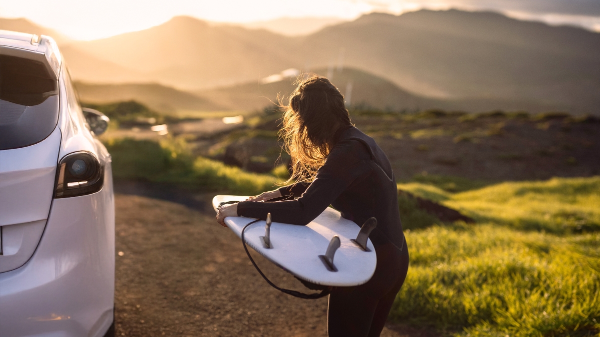 surfer holding surfboard standing next to electric vehicle