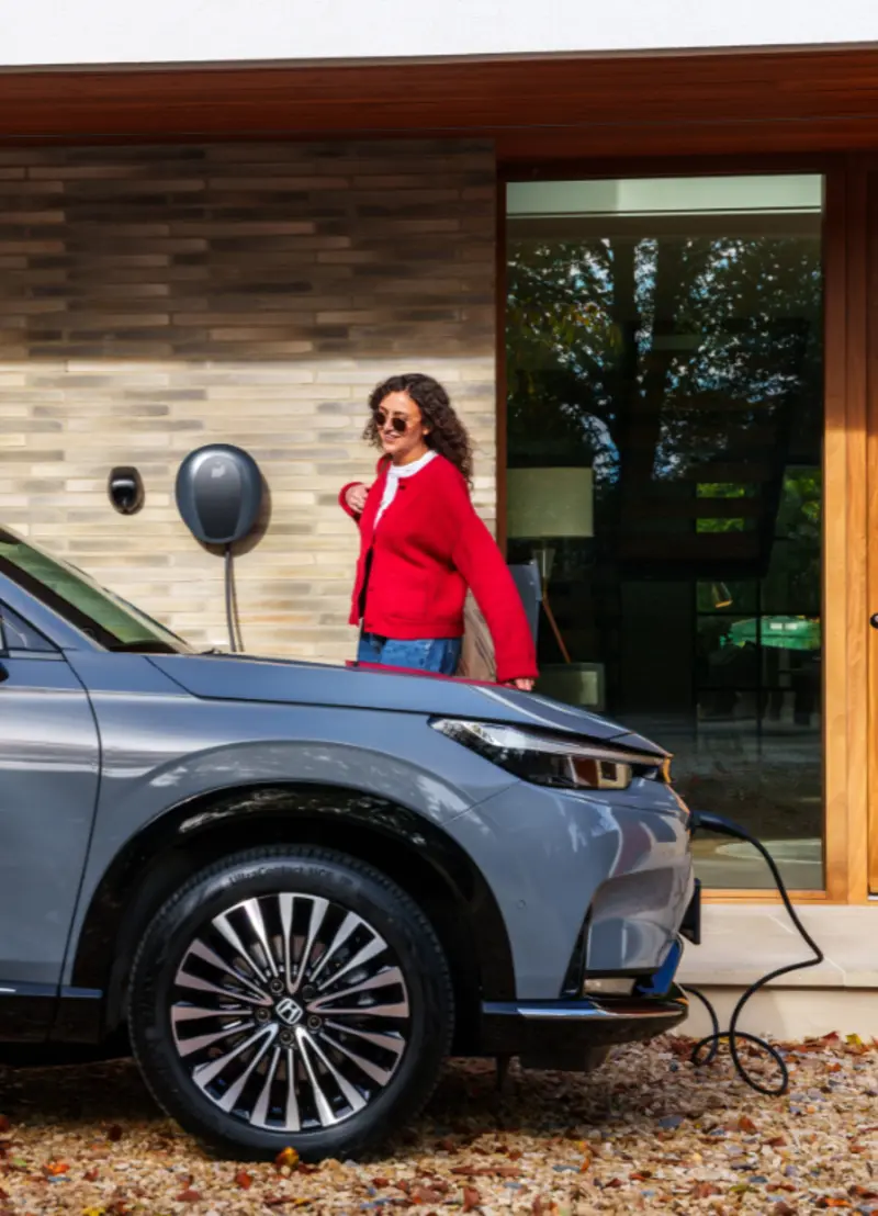 lady walking to car whilst pod point tethered unit charges her EV