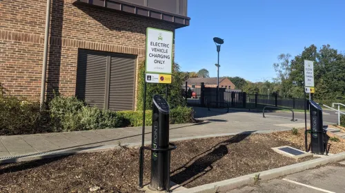 A diagonal shot of two Pod Point twin chargers with signage above them, in front of Merchant Taylor's school